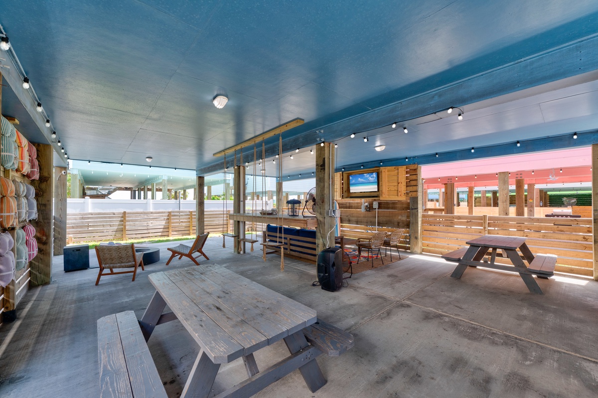 Relax under the bright blue ceiling in this inviting covered patio, where picnic tables and comfy seating offer the perfect spot to unwind and gather with friends.