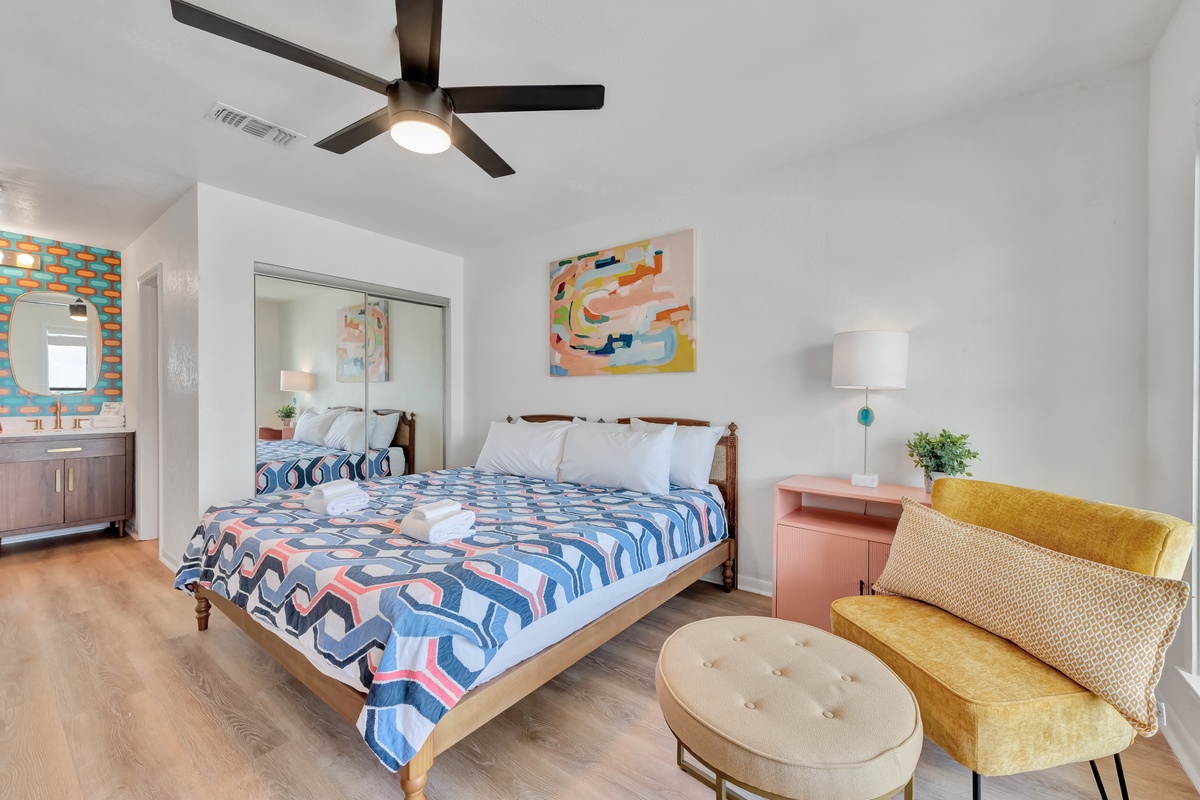 Relax in your stylish bedroom with vibrant décor, ceiling fan, and cozy seating nook perfect for unwinding.
