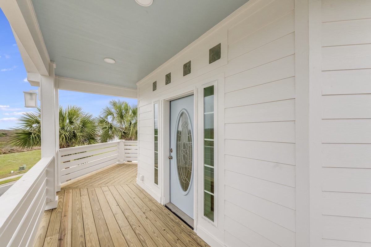 Charming coastal entrance welcomes you with white shiplap siding and covered porch overlooking palm trees and open fields.