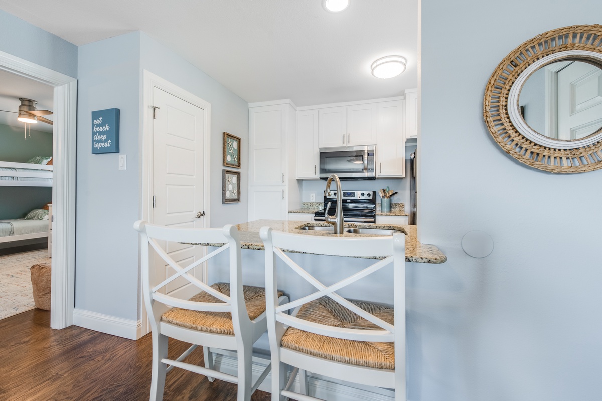 Your coastal kitchen invites morning coffee at the breakfast bar, where soft blue walls and white cabinets create a serene cooking space.