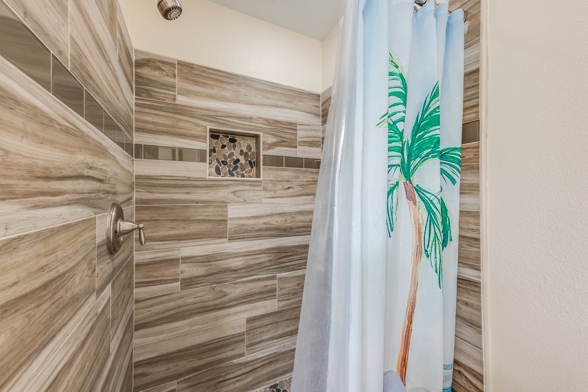 Step into your tropical-themed shower featuring stunning wood-grain tiles and a charming palm tree curtain for beachy vibes.