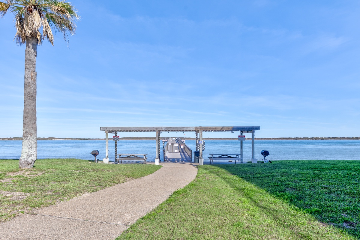 Waterfront pavilion with private dock access overlooking tranquil bay waters, surrounded by manicured lawns and tropical palms.