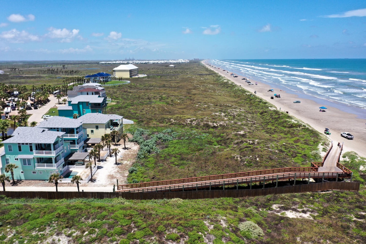 Aerial view showcasing beachfront properties with direct boardwalk access to pristine sandy shores and rolling ocean waves.