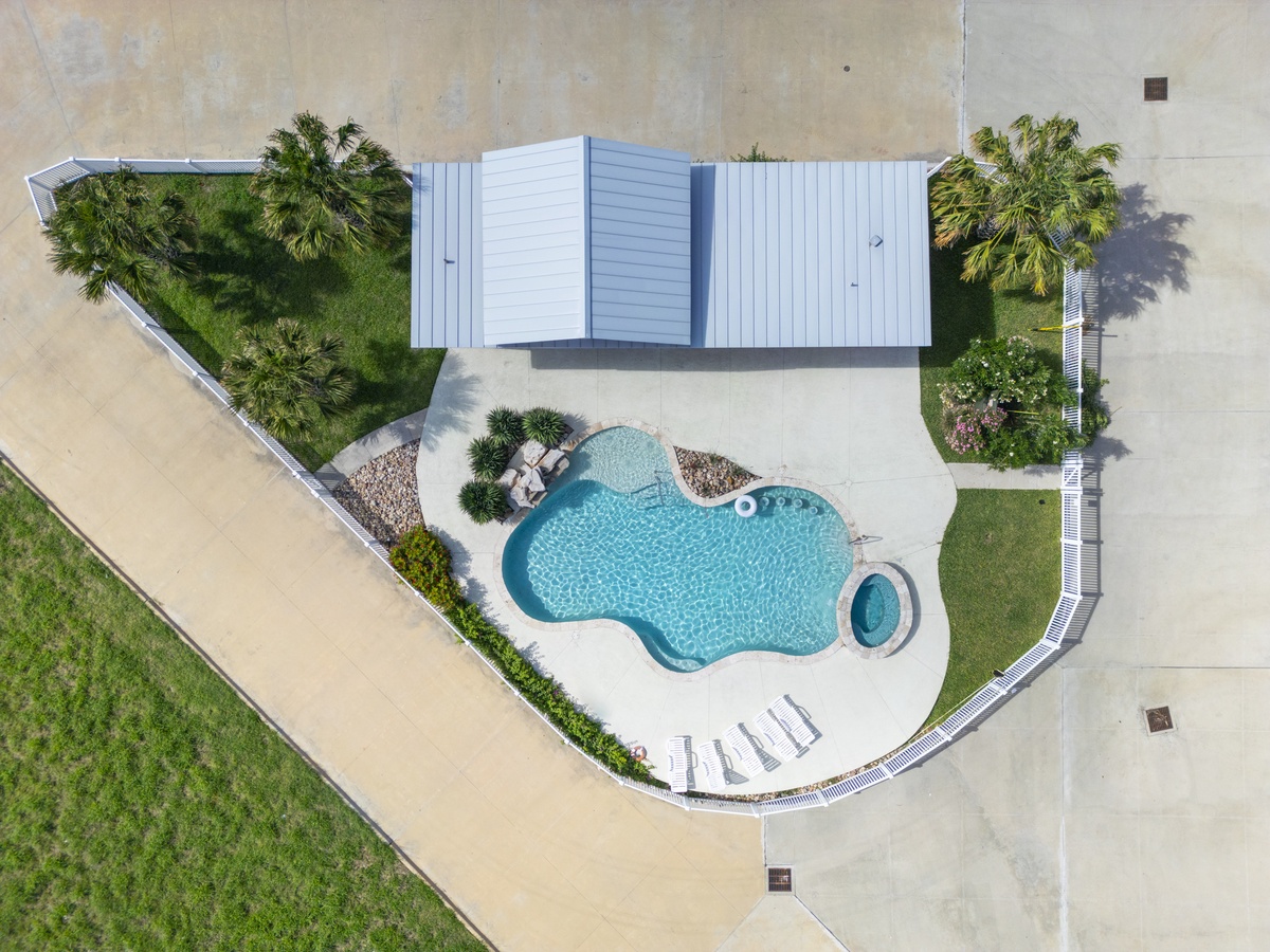 Aerial view of the property's stunning pool area and tropical gardens with palm trees and outdoor seating.