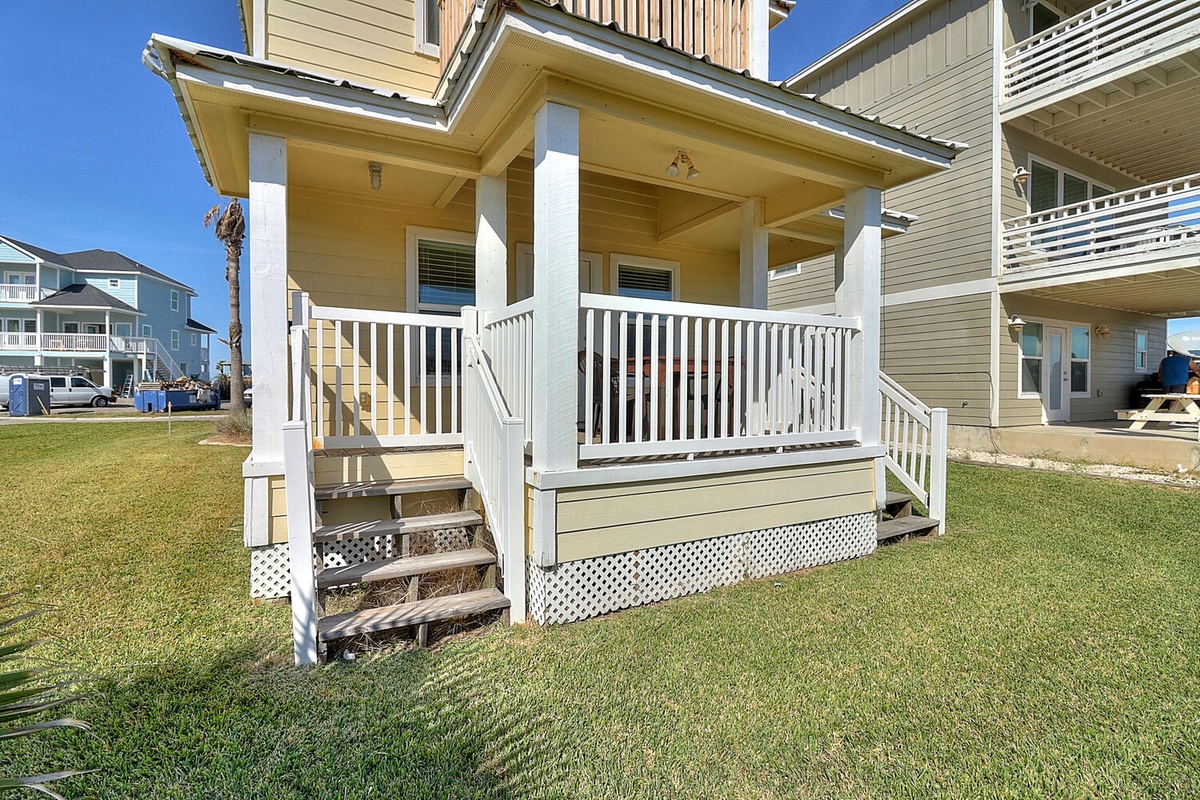 Charming beach house with covered porch and white railings in coastal neighborhood surrounded by green lawn.
