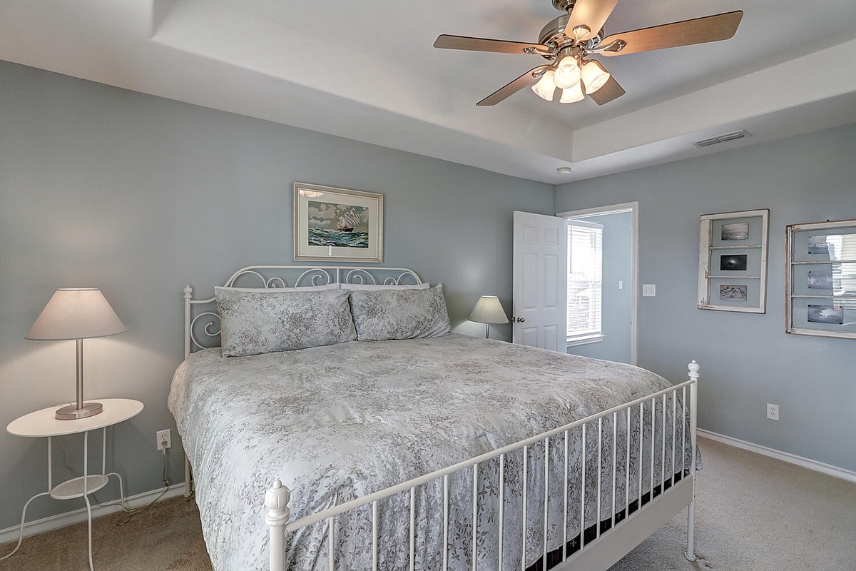 Drift off to sleep in this peaceful bedroom with soft blue walls, crisp white linens, and a gentle ceiling fan to keep you comfortable all night.