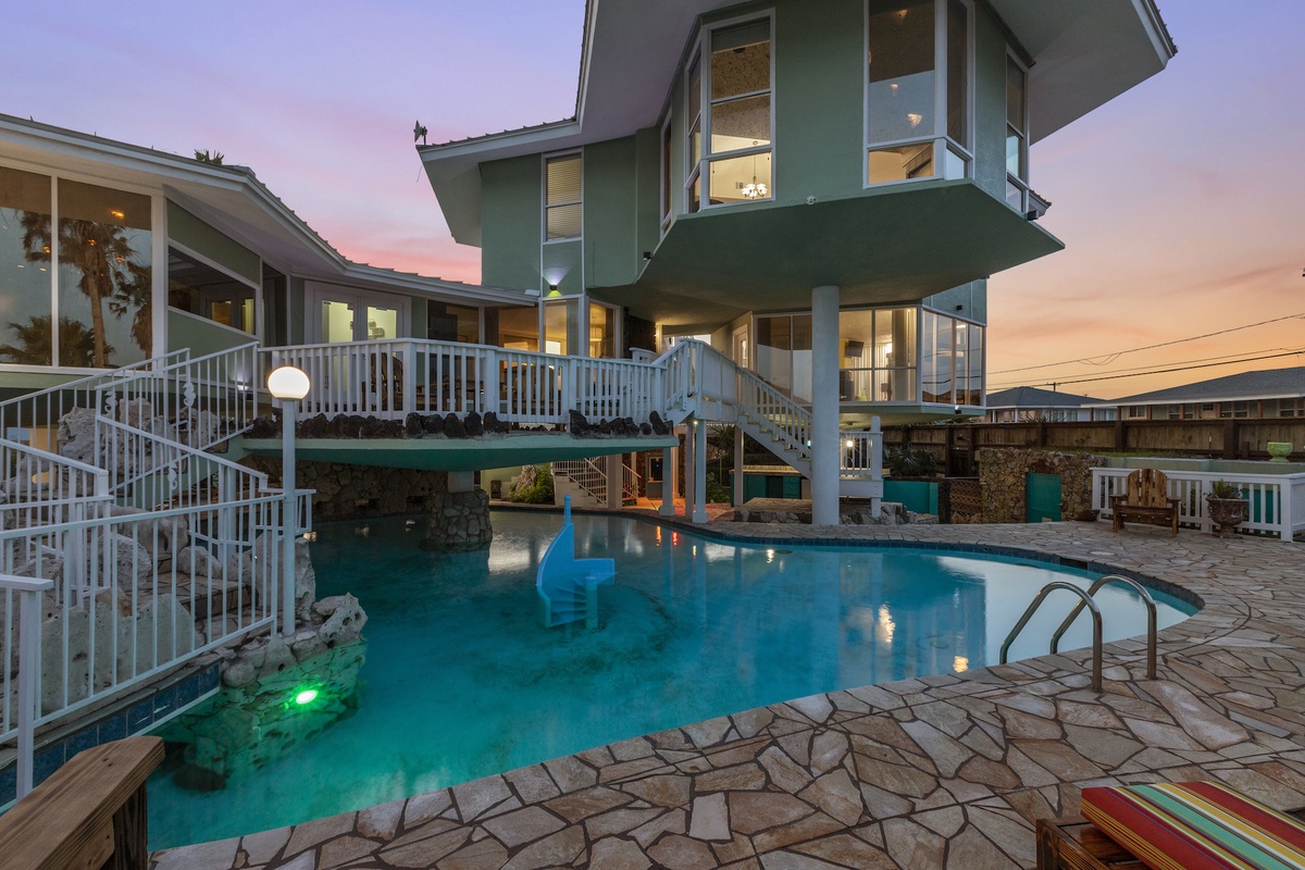 Stunning vacation home with illuminated pool at twilight, featuring elevated walkways and panoramic views.