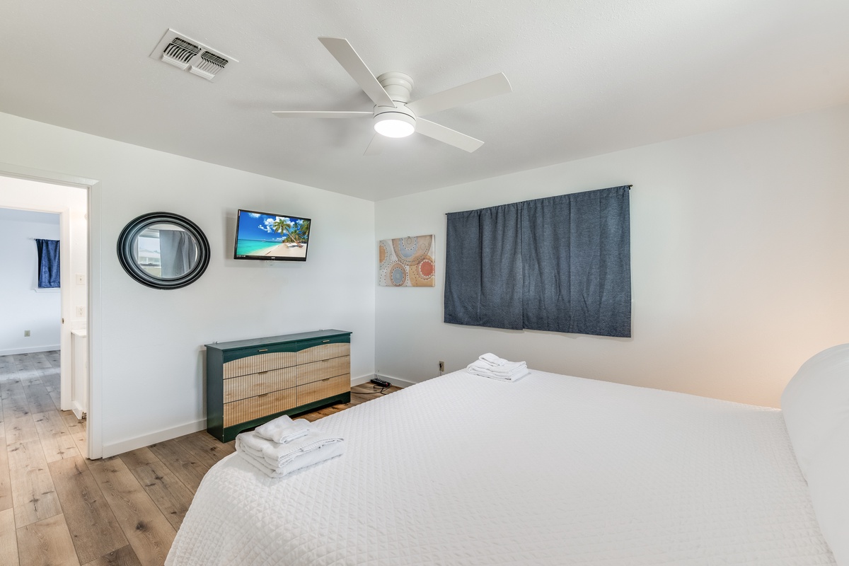 Rest comfortably in your bright bedroom with crisp linens, modern amenities, and tropical artwork creating a peaceful retreat.