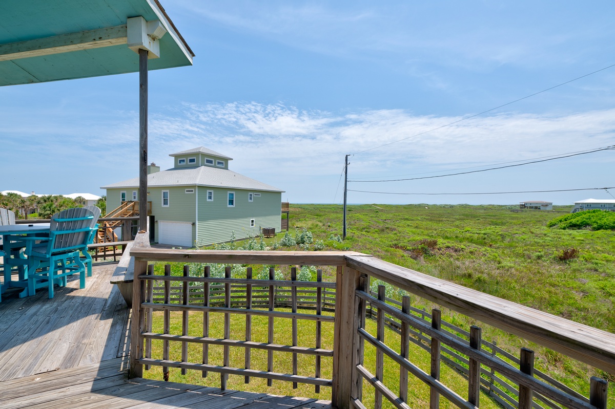 A covered deck with coastal charm overlooks natural dunes and neighboring beach homes, offering a peaceful setting for seaside relaxation.