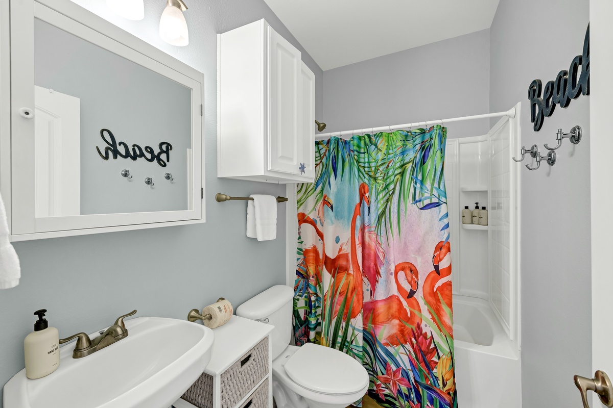 Step into your tropical oasis with vibrant flamingo shower curtain, peaceful blue walls, and thoughtful touches that make this bright bathroom feel like home.