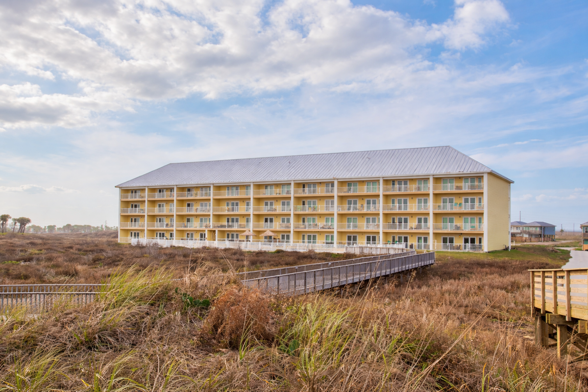 Beachfront property featuring multiple balconies and direct dune access via wooden walkway, surrounded by natural coastal landscape.