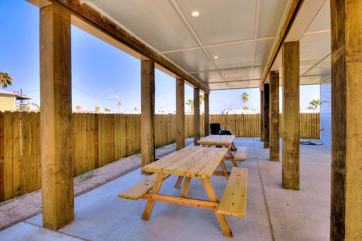 Your covered patio offers a perfect shaded retreat with picnic tables and BBQ setup, ideal for outdoor dining and grilling.