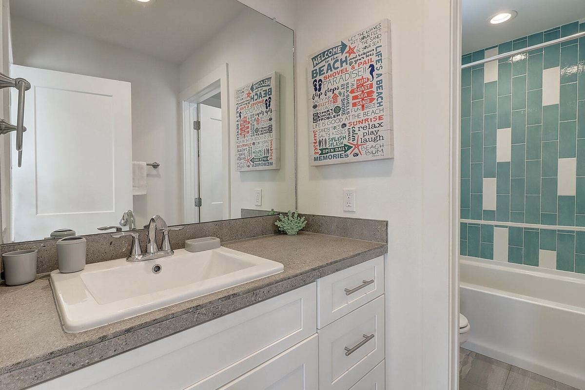 Refresh after beach days in your bright, modern bathroom with coastal artwork and cheerful turquoise tile details.