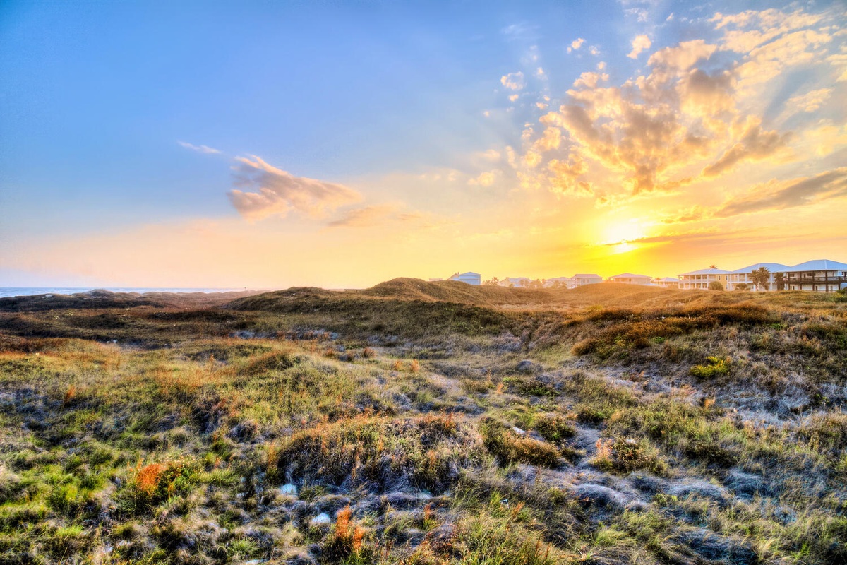 Spectacular sunset over coastal dunes with vacation properties nestled in the natural landscape.