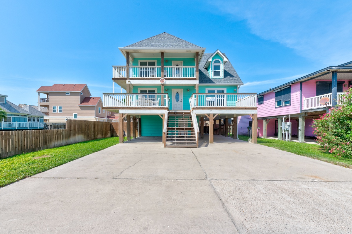 Charming turquoise beach house with multiple balconies sits in a vibrant coastal neighborhood with colorful homes nearby.