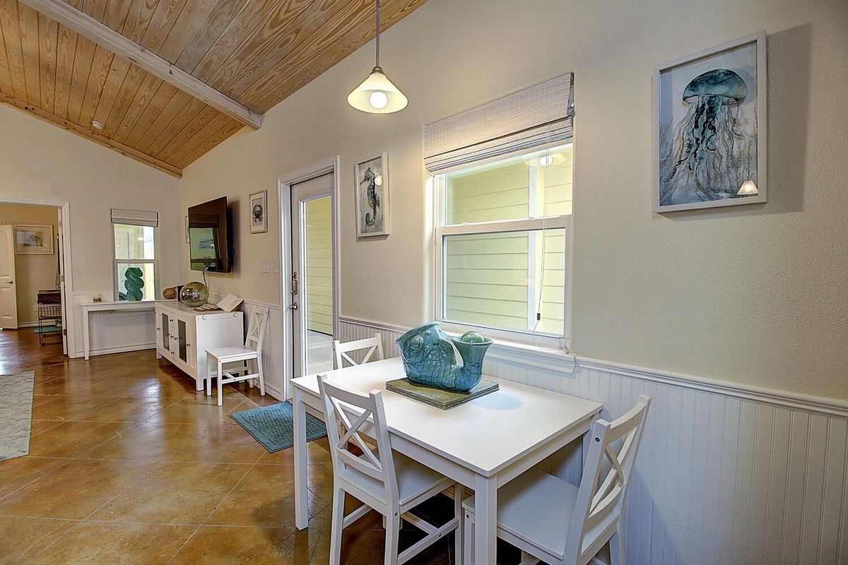 Gather around your charming dining table beneath warm wood-beam ceilings, where coastal artwork and natural light create the perfect breakfast nook.