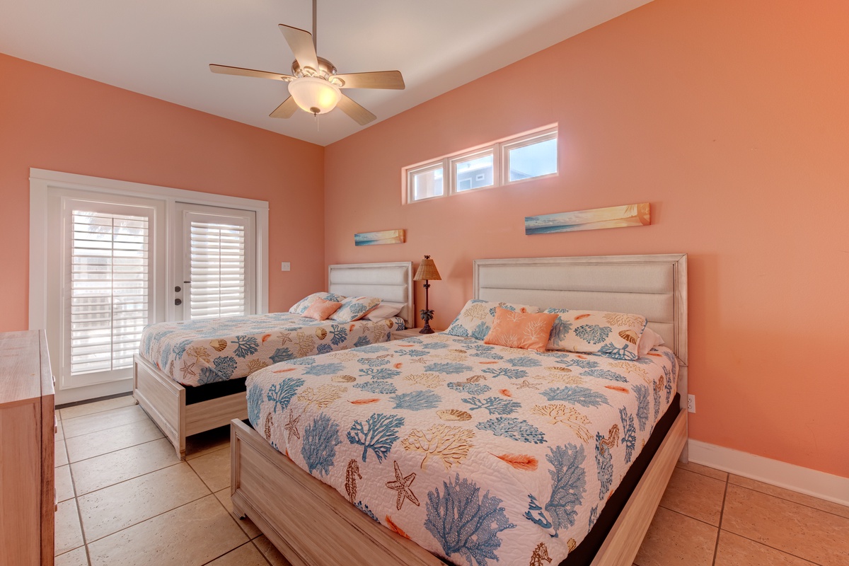 Drift off to sleep in your coastal-themed bedroom with twin beds, ceiling fan, and cheerful coral walls that evoke sunset beach vibes.