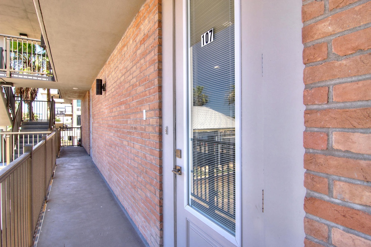 Exterior walkway with brick architecture leading to unit 107, featuring covered access and convenient street-level entry.