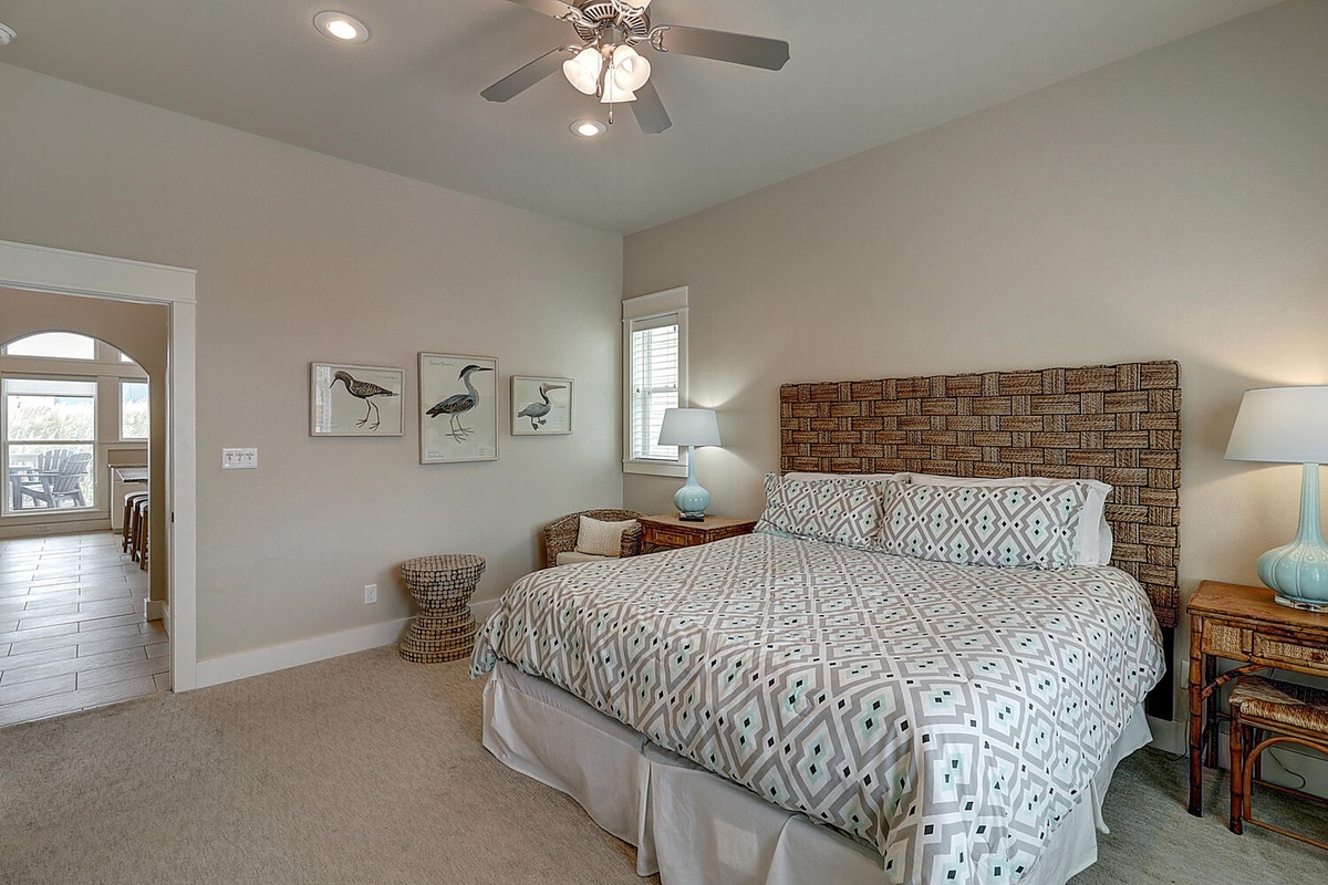 Drift off in your serene bedroom featuring coastal bird art, wicker accents, and soft linens beneath a gentle ceiling fan.