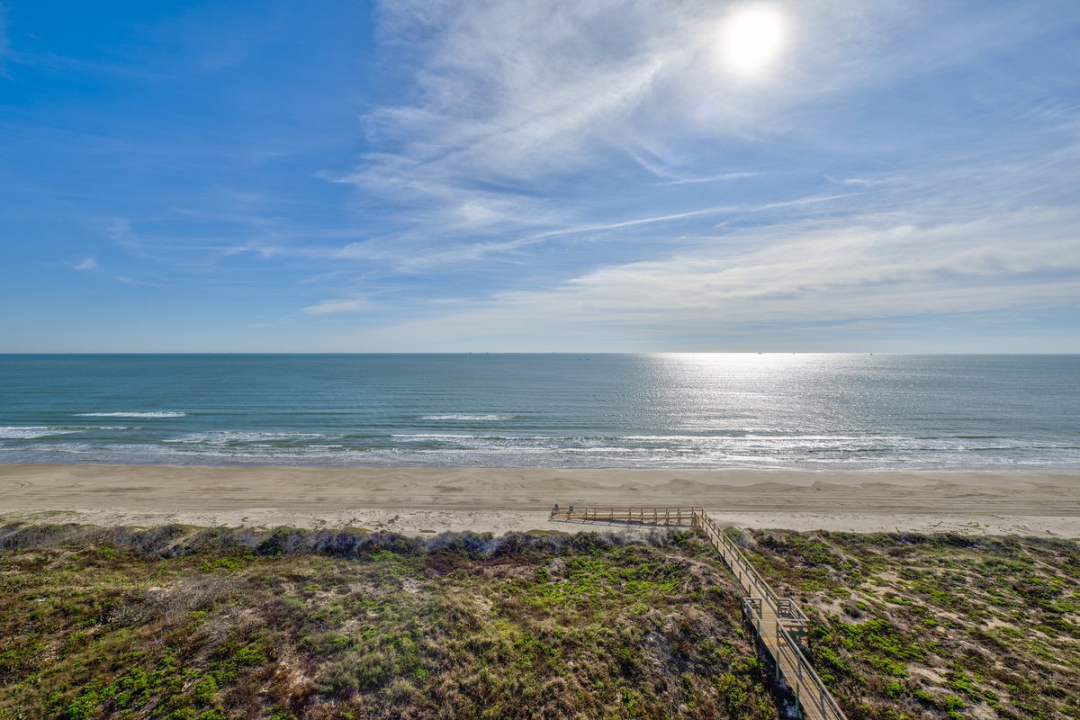 Panoramic ocean view with pristine sandy beach and wooden boardwalk winding through coastal dunes under bright blue skies.