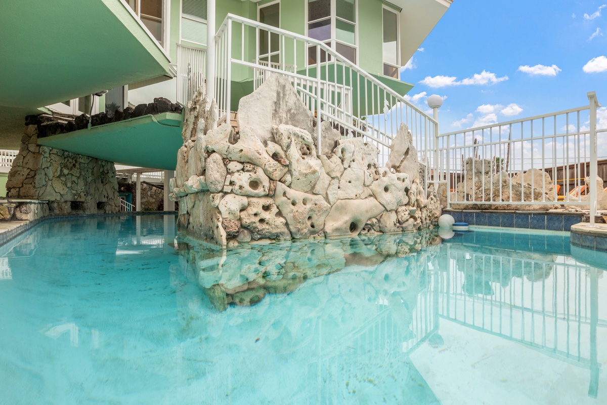 Dive into crystal-clear waters surrounded by stunning rock formations and tropical architecture under bright blue skies.