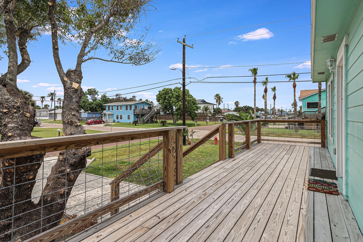Step onto your private deck with wooden railings overlooking a peaceful neighborhood dotted with colorful coastal homes and swaying palms.