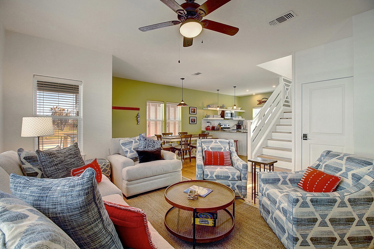 Unwind in your bright living room with cozy blue seating, colorful pillows, and an open layout connecting to the kitchen.