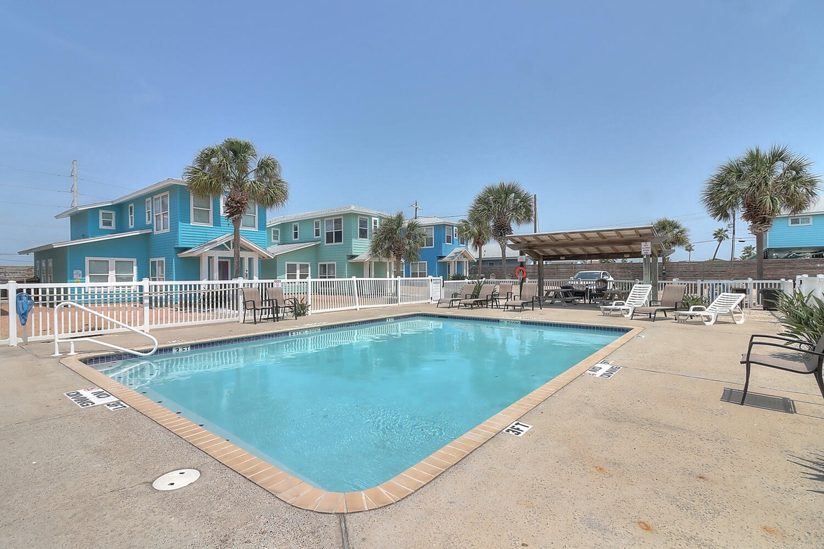 Turquoise beach houses and palm trees frame this inviting pool area, perfect for coastal relaxation.