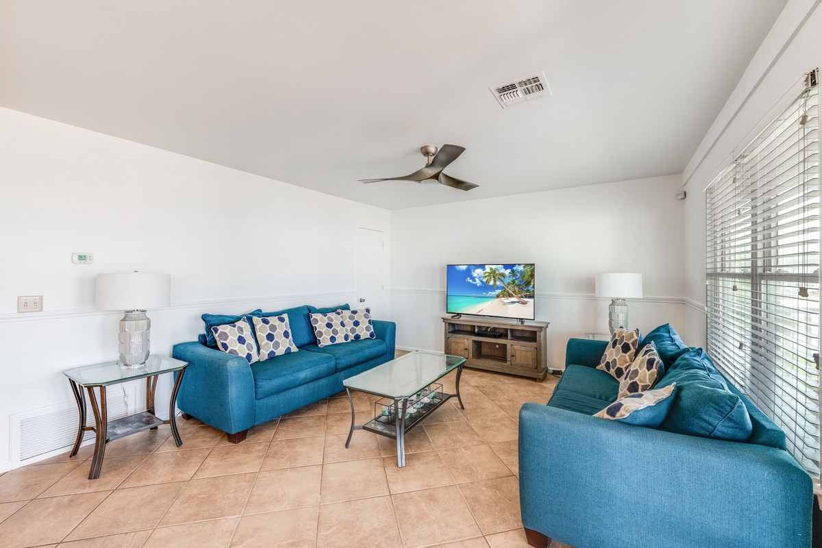 Unwind in your bright living space with plush turquoise seating, modern entertainment, and cooling ceiling fan for ultimate relaxation.