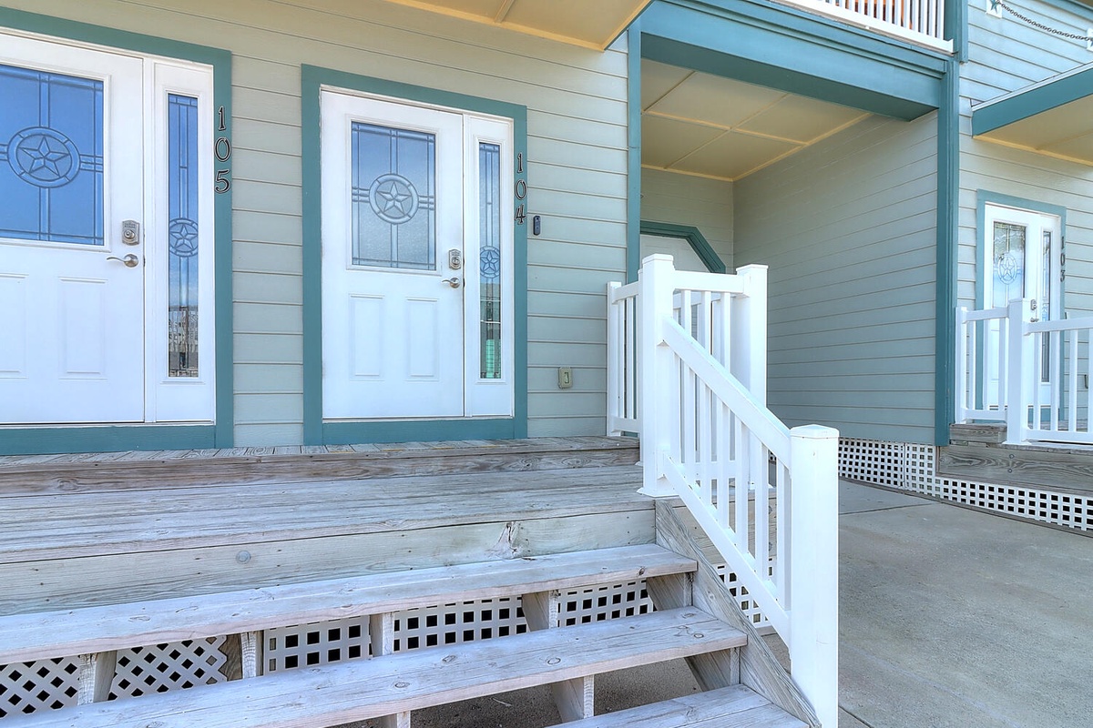 Charming coastal-style property entrance with covered walkways and multiple units featuring nautical-themed front doors.