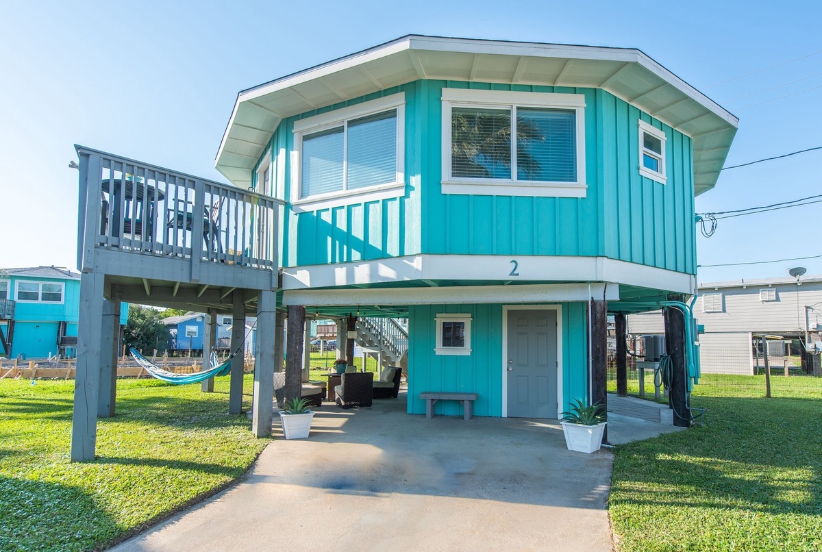 Charming turquoise beach house with elevated deck and hammock for relaxing coastal getaways.