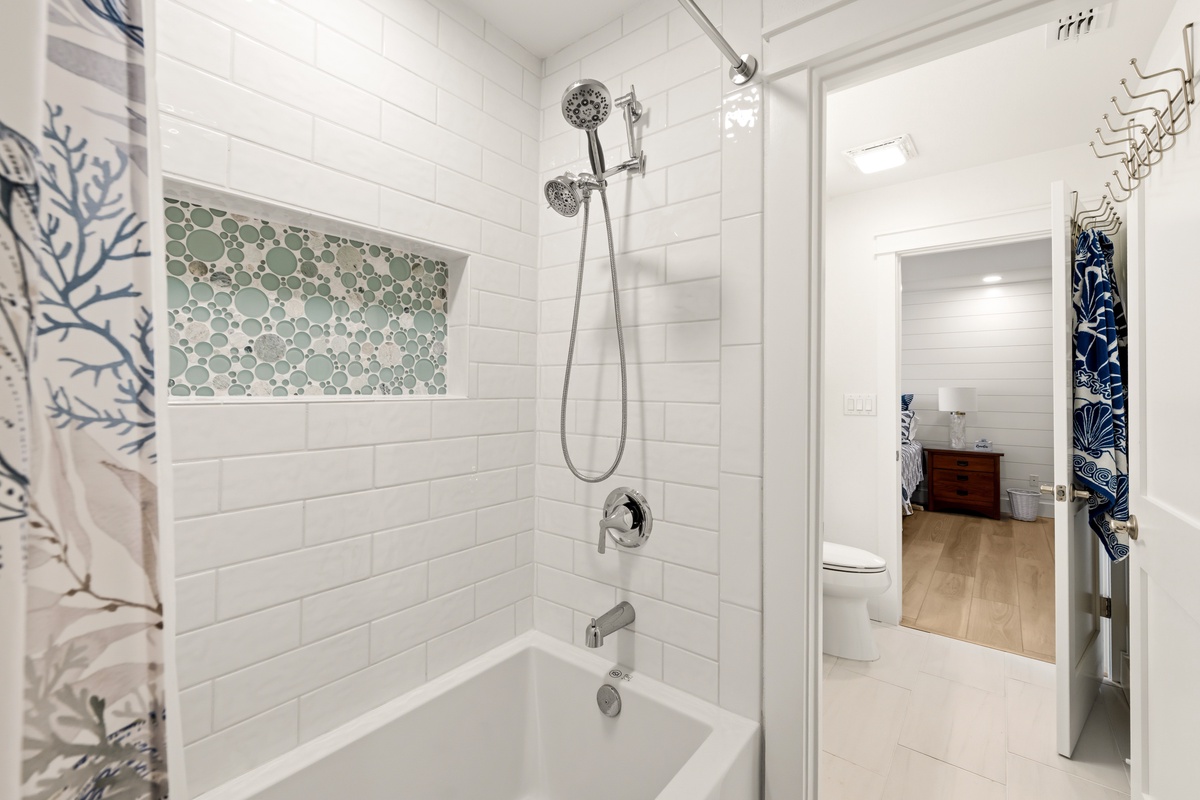 Your private bathroom features a sleek tub-shower combo with subway tile walls and a soothing sea-glass mosaic accent niche—perfect for unwinding after a day of exploring.