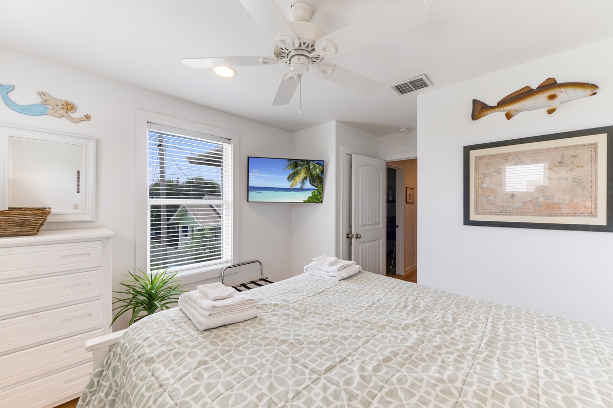 Unwind in your coastal-themed bedroom, where a ceiling fan keeps you cool and crisp linens await. Natural light fills the space, making relaxation effortless.