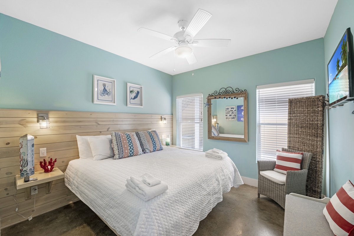 Relax in this bright and inviting bedroom, featuring a comfortable bed, cheerful coastal décor, and plenty of natural light.