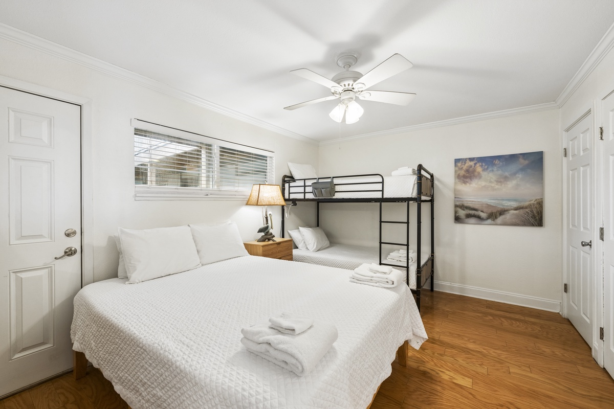 Settle into crisp white linens and coastal charm. Your serene bedroom features warm hardwood floors, gentle ceiling fan, and a beach scene that brings the shore indoors.
