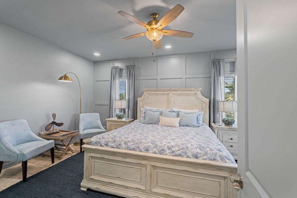 Sink into your elegant bedroom retreat featuring a plush king bed, cozy reading chairs, and gentle ceiling fan for perfect comfort.