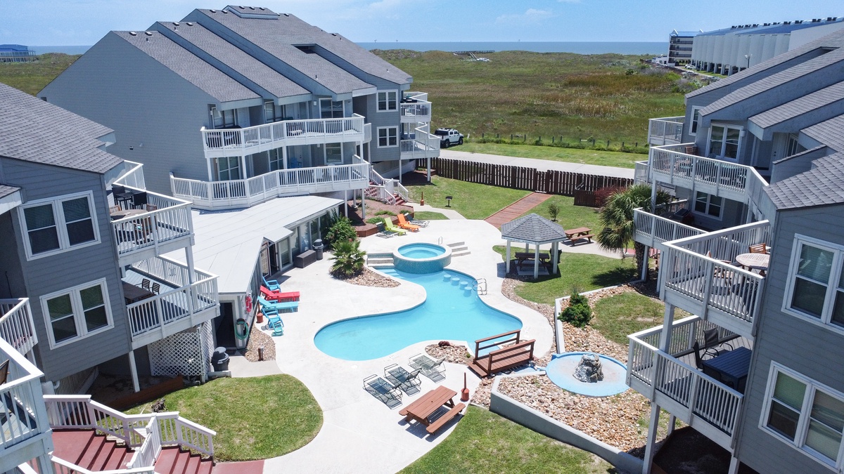 Aerial view of beachside vacation rental complex with private pool, hot tub, and multiple oceanfront units surrounded by coastal landscape.
