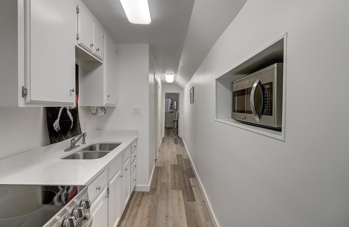 Step into your sleek galley kitchen featuring stainless steel appliances, pristine white cabinetry, and modern flooring that flows throughout your space.