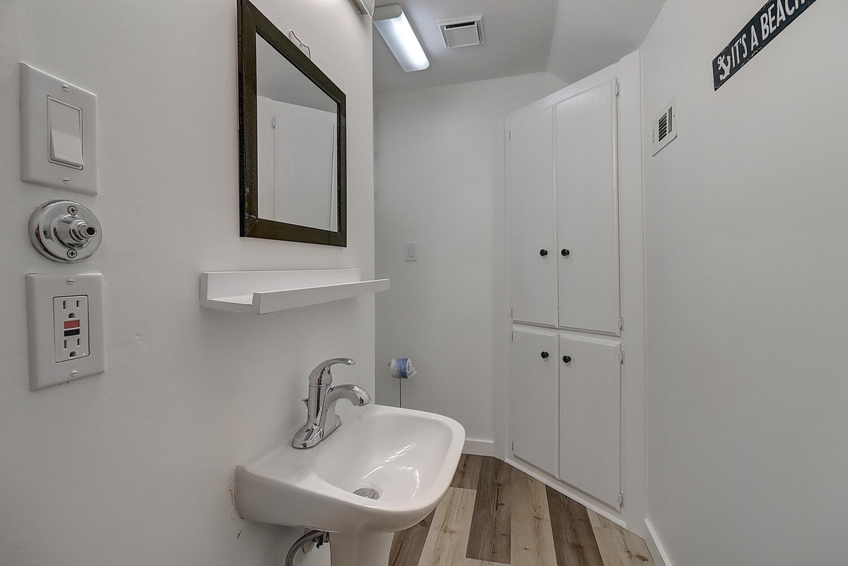 Your stylish bathroom offers modern convenience with a sleek sink, framed mirror, and ample storage in bright white cabinets.
