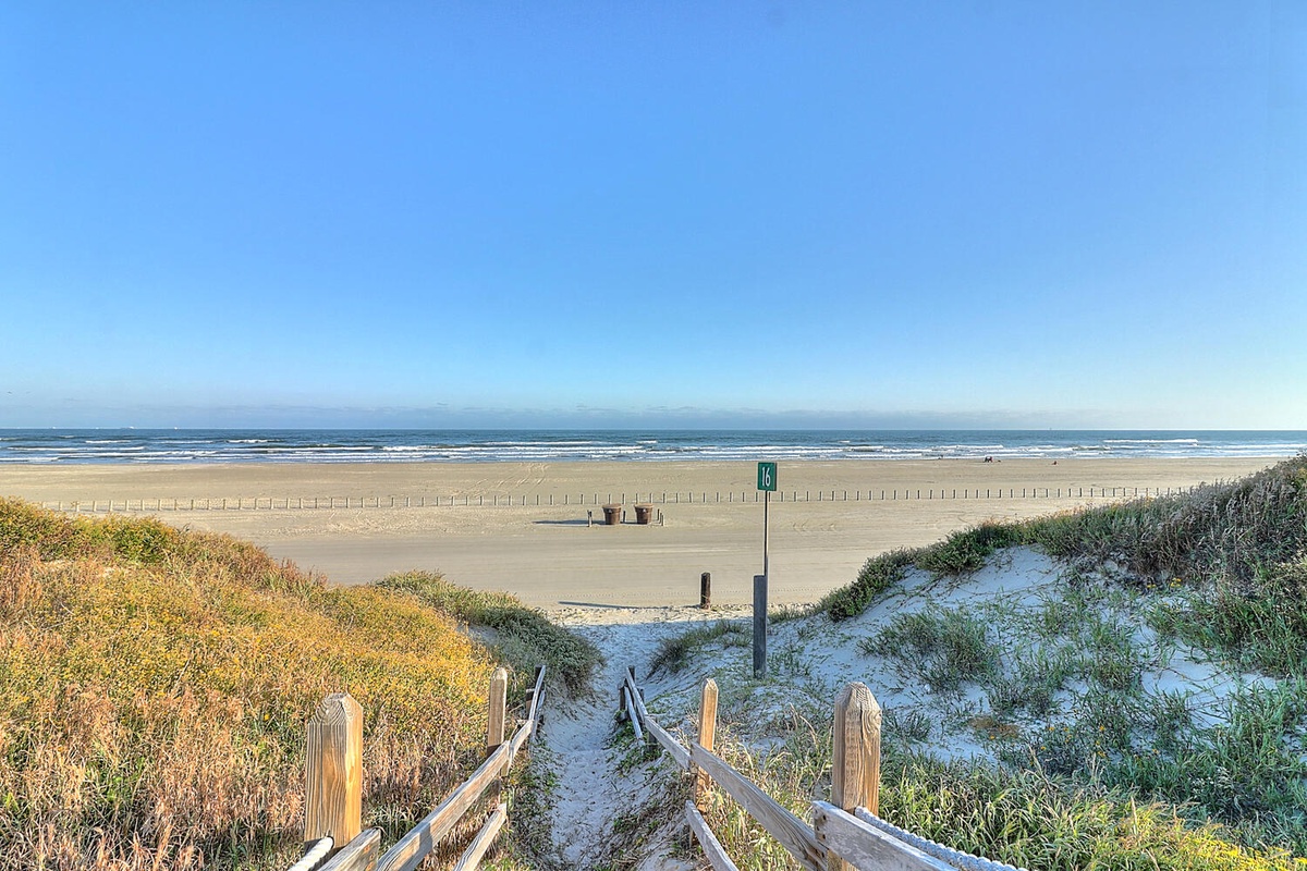 Expansive sandy beach stretches along the coastline with gentle waves and clear blue skies creating a peaceful coastal setting.