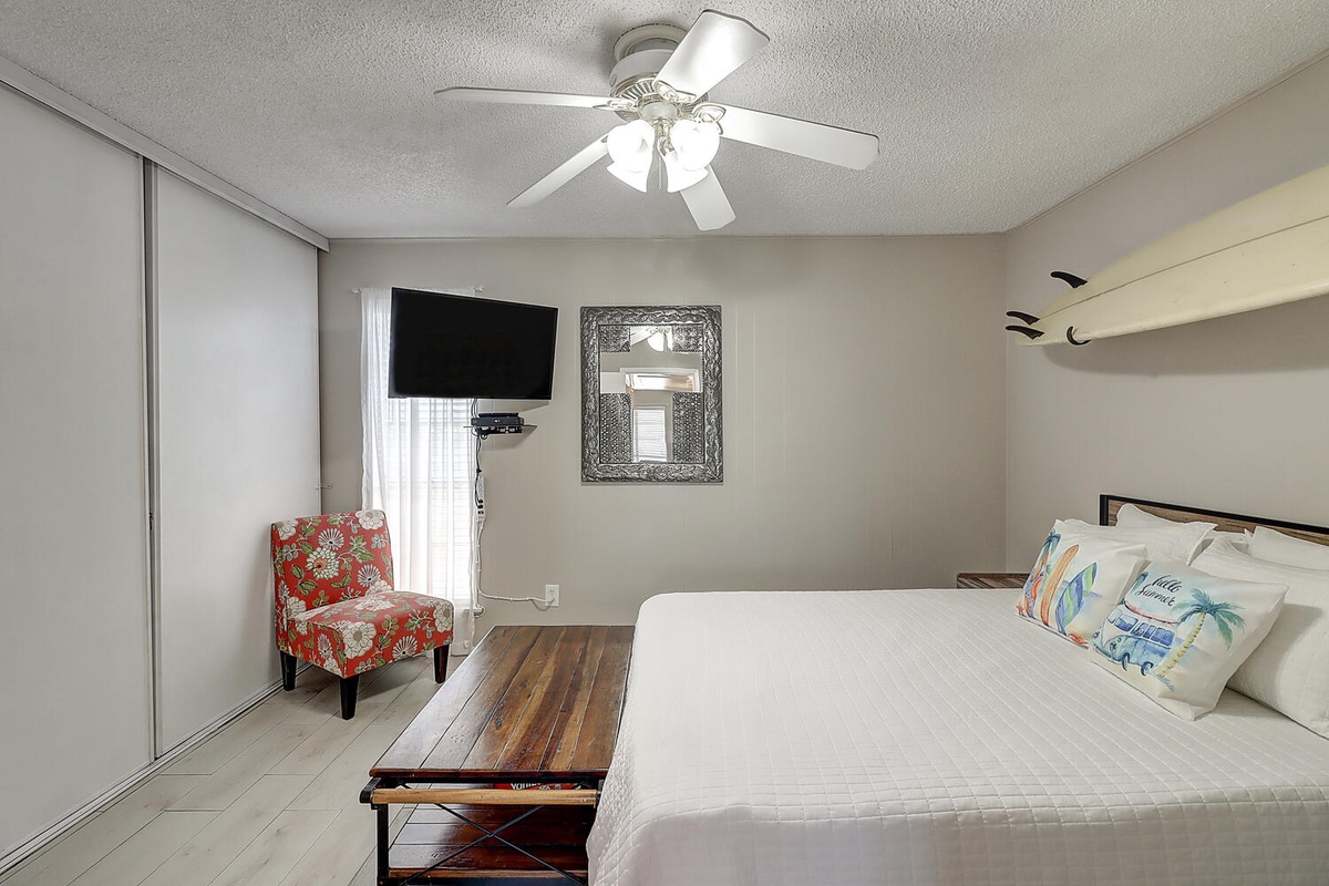 Unwind in your comfortable bedroom with plush bedding, wall-mounted TV, and cooling ceiling fan for perfect relaxation.