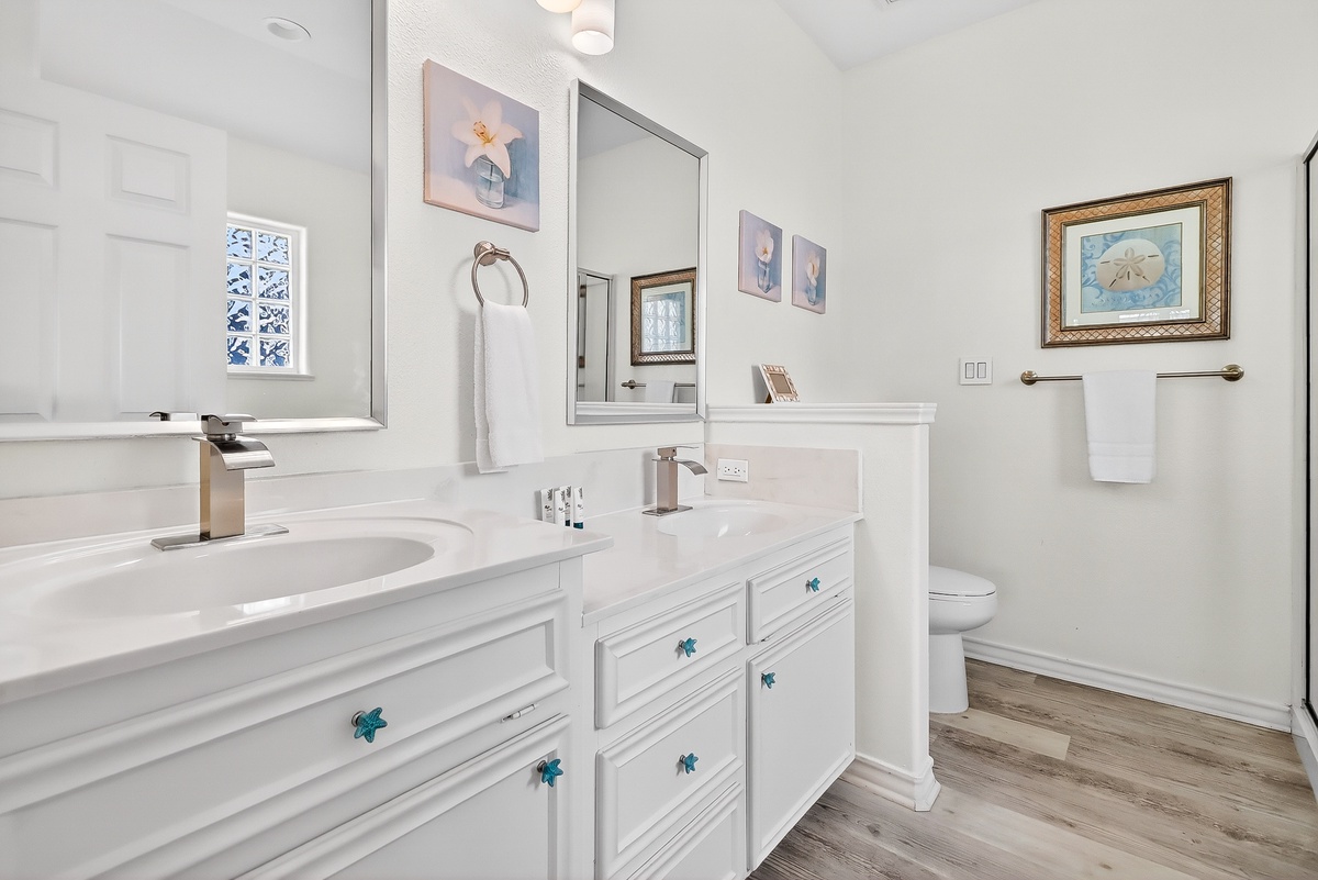 Unwind in your pristine bathroom featuring elegant marble counters, coastal-themed artwork, and luxurious amenities for your perfect getaway.