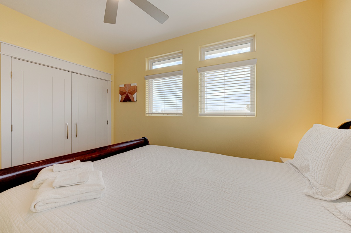 Rest peacefully in your bright, cheerful bedroom with sunny yellow walls, ceiling fan, and fresh white linens waiting for your arrival.