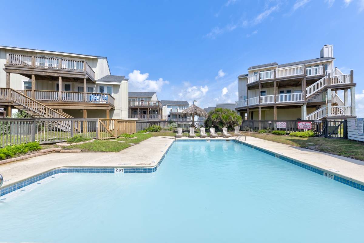 Dive into your private retreat—a sparkling community pool framed by coastal villas, sun loungers waiting, and ocean breezes just beyond the dunes.