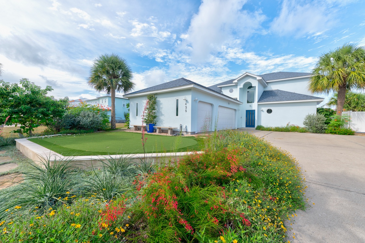 A spacious vacation home with inviting tropical landscaping and a private putting green, set in a tranquil residential area with palm trees and vibrant flowers.