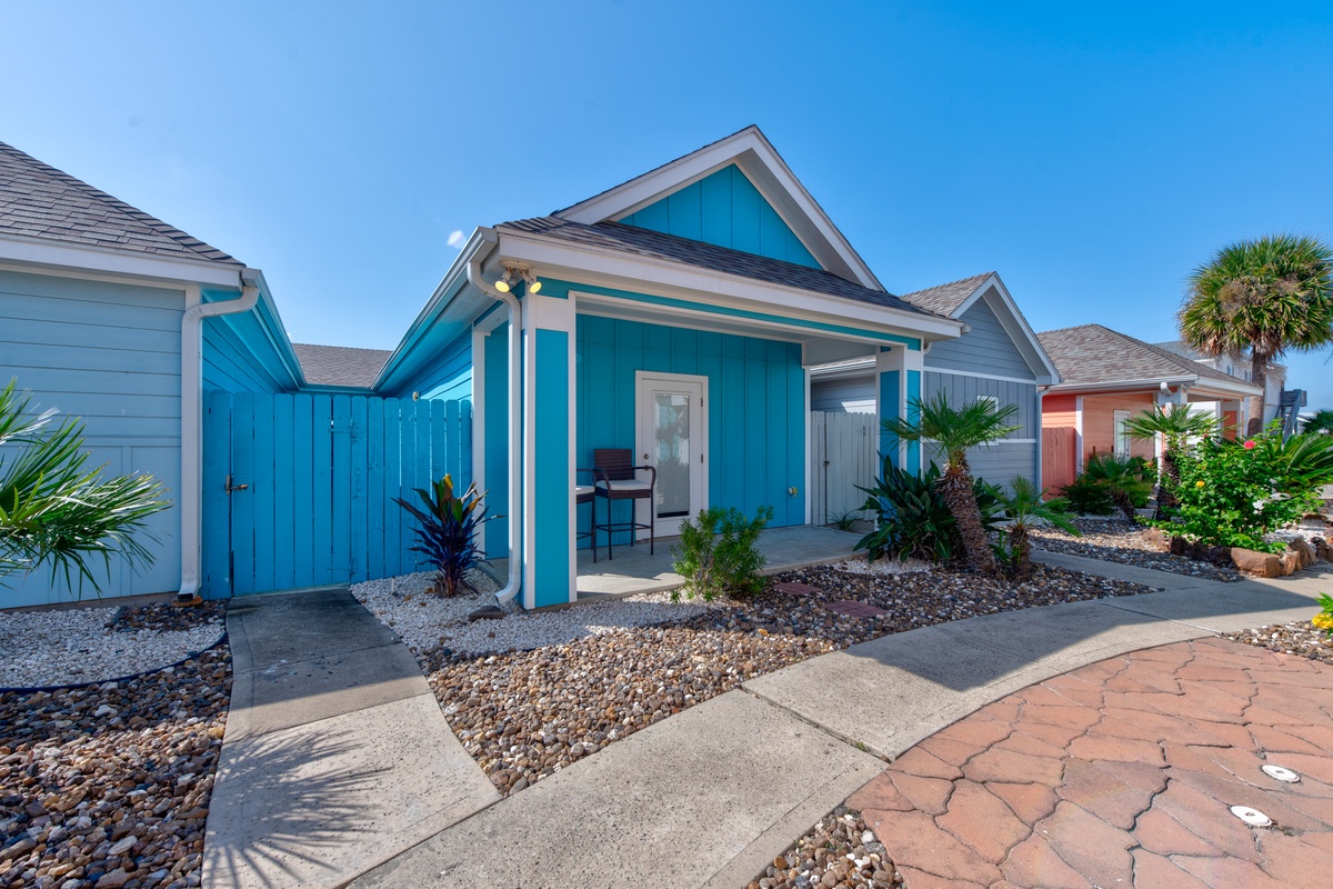 Bright turquoise cottage with tropical landscaping and paved walkways in a charming coastal community setting.