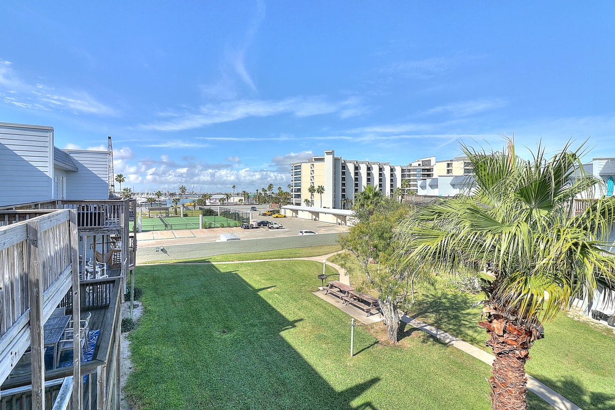 Beachfront community setting with palm trees and green spaces stretching toward coastal hotels under bright blue skies.