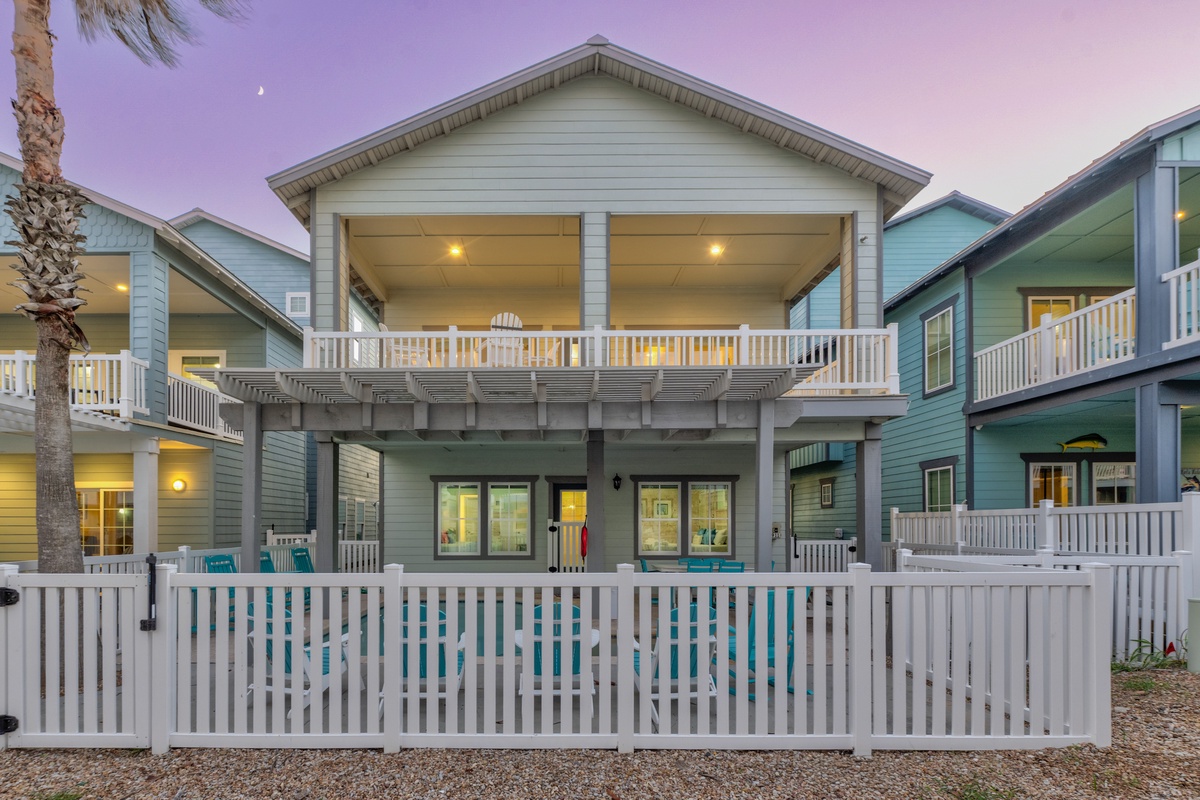 Charming beach house with covered porches and coastal design, surrounded by similar vacation homes in a peaceful neighborhood setting.