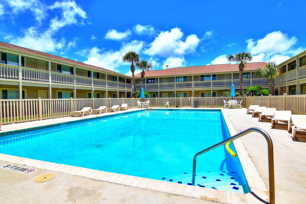 This inviting outdoor pool area features crystal-clear waters surrounded by comfortable loungers, perfect for soaking up sunshine under beautiful blue skies.