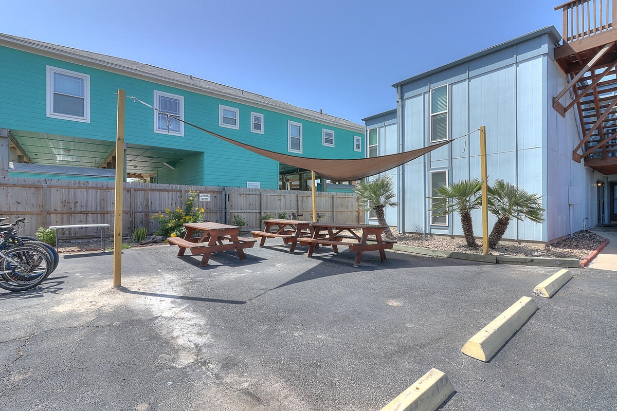 Colorful beach-style buildings create a vibrant coastal community setting with shaded outdoor dining areas and convenient bike storage.